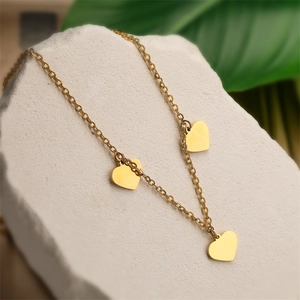 Close-up of golden stainless steel necklace with heart pendants on a white stone base