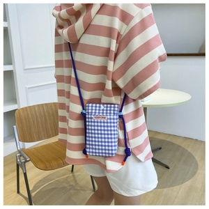 Detail of purple checkered crossbody bag with adjustable strap worn on striped hoodie