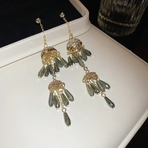 Detail of gold butterfly tassel earrings with emerald beads and pearls in close-up view
