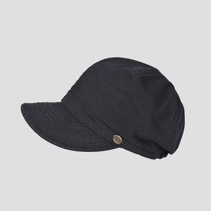 Detailed macro view of black cotton newsboy hat featuring a bronze metal badge on the side