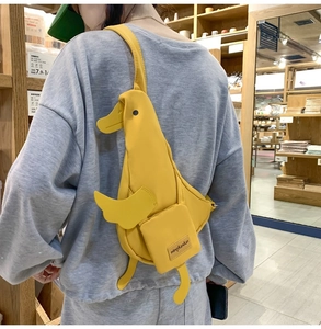Detail of yellow duck-shaped crossbody bag worn by a model in a casual store setting