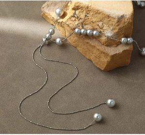 Detail of grey pearl necklace draped on natural stone showing fine silver chain texture