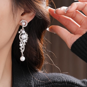 Detailed view of silver needle pearl drop earrings with rhinestones on a model