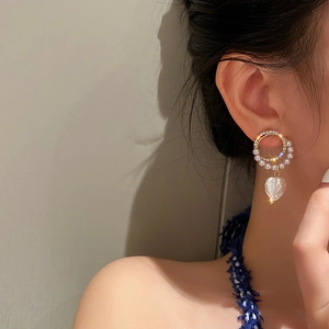 Detail of double hoop pearl earrings with a sparkling heart pendant worn by a model