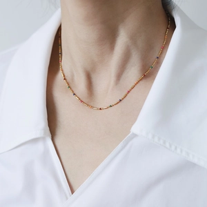 Detail of 18K gold-plated rainbow necklace with colorful beads on a white shirt