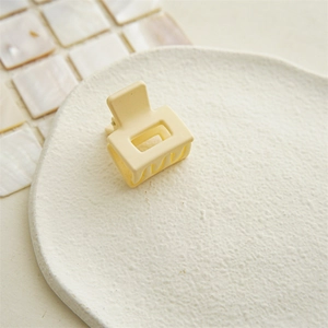 Close-up of matte yellow square hair claw clip on a white tray with shell tile background