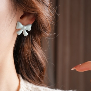 Detail of light blue bow stud earring worn on ear with soft knit sweater background