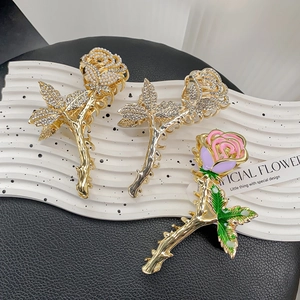 Elegant gold rose hair claw clips with rhinestones and pearls on white wavy tray