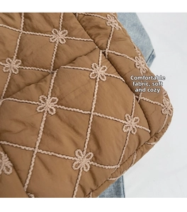 Detail of brown quilted fabric with diamond pattern and small embroidered flowers on tote bag