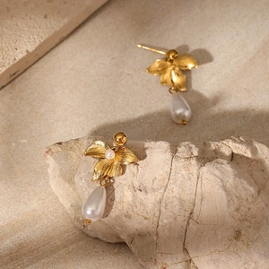 Detailed close-up of gold-plated floral earrings with white teardrop pearls on a stone