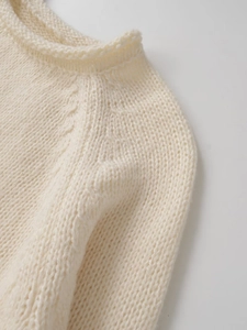Detail des Grobstrick-Ausschnitts und der flauschigen Textur eines cremefarbenen Pullovers