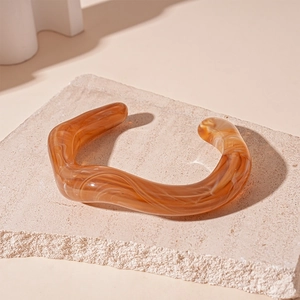 Macro detail of amber resin wavy open cuff bracelet with white marble texture on stone base