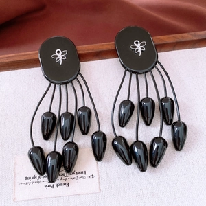 Détail de boucles d'oreilles ethniques noires avec décor d'insecte et glands perlés