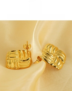 Detailed view of square gold earrings with woven texture on yellow satin fabric