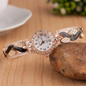 Close-up of women's gold quartz watch with rhinestones and leaf pattern on a rock