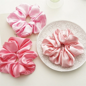 Detailed view of three large pink satin scrunchies with glossy texture on a ceramic plate