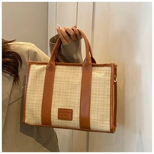 Detail view of woven straw tote bag with brown leather trim and metallic strap hooks