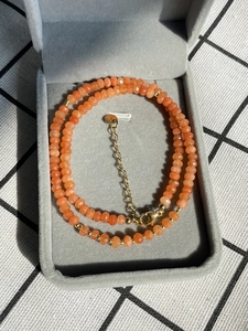 Detail einer Halskette aus orangefarbenem Naturstein mit vergoldeter Kette im Etui