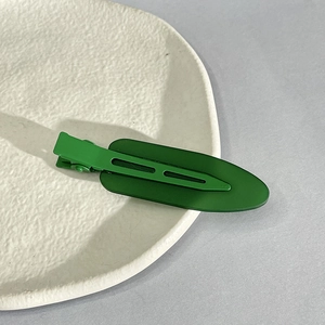 Close-up of a matte green duckbill hair clip on a textured ceramic dish in natural light