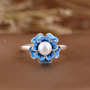 Macro shot of silver irregular ring with blue enamel flower and white pearl detail