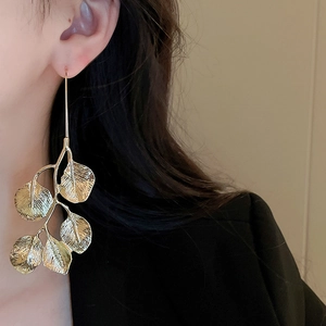 Detail of a golden leaf earring on a model featuring intricate metallic textures