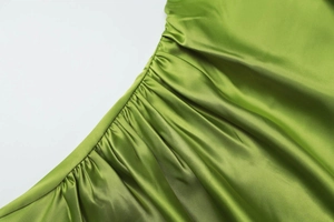 Detailed view of green satin fabric with smooth glossy finish and pleated texture detail