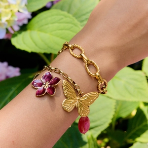 Two-piece layered gold link bracelet with purple flower and butterfly charms on wrist