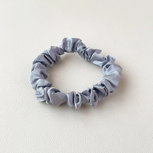 Macro shot of silver satin fabric scrunchie texture with silky smooth reflections