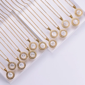 Gold letter pendant necklaces with rhinestones and white shell inlay displayed on a rack
