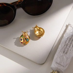 Macro shot of gold ladybug stud earrings with multicolored zircons on a laptop