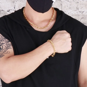 Close-up of golden Figaro chain necklace and bracelet set worn by male model