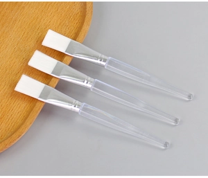 Close-up of three facial mask brushes with white bristles and transparent handles