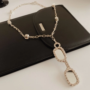 Detail of silver long chain necklace with a zircon-encrusted eyewear pendant on black leather