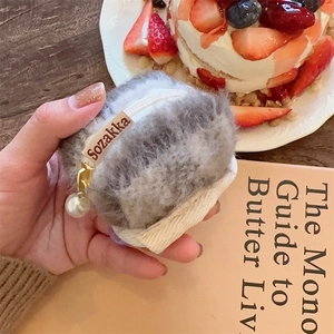 Close-up of grey plush AirPods case with a gold pearl zipper and a side brand label