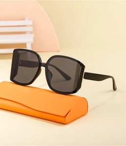 Detail of oversized black sunglasses with gold accents and bright orange case
