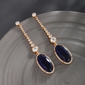 Detailed macro view of gold-plated drop earrings featuring navy blue oval gemstones