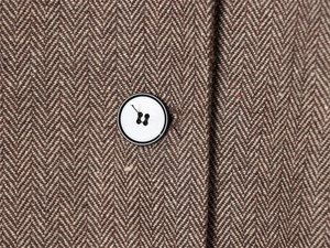 Macro shot of coffee brown herringbone wool fabric and a black four-hole button detail