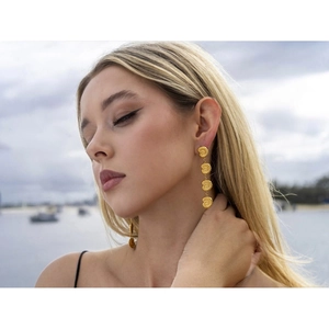 Detail of elegant 18k gold conch shell drop earrings worn in a beach setting
