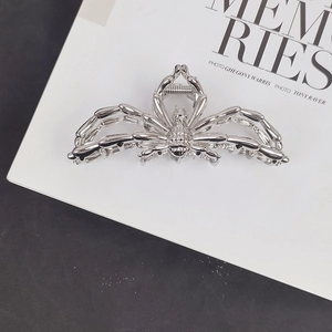 Top-down view of a large silver metal spider hair claw clip on a white magazine background