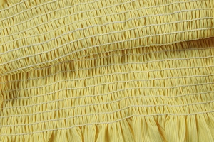 Vue détaillée de la texture du tissu smocké jaune avec coutures élastiques extensibles