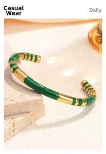 Detailed view of emerald green enamel and gold plated stainless steel open bangle on stone