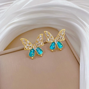 Close-up of blue butterfly stud earrings with gold plating and cubic zirconia detailing