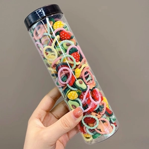 Close-up of colorful fruit shaped elastic hair bands in a clear plastic jar with black lid