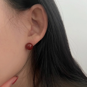 Close-up of 925 sterling silver stud earring with dark red spherical bead on a model