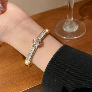 Detailed view of luxury gold bangle with zircon flower on a model wrist with black suit