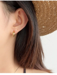 Close-up of minimalist golden hoop earring on model with summer straw hat background