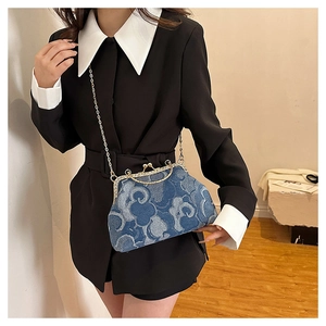 Detail of blue denim kiss-lock bag with cloud print and gold chain strap held by model