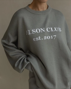 Detailed view of the ribbed crew neck and white Alson Club embroidery on the gray sweater