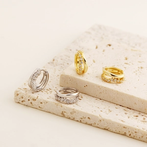 Detail of silver and gold double-layered huggie earrings with cubic zirconia inlay on stone
