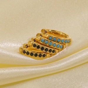 Elegant gold huggie earrings with turquoise and black gemstones on cream satin fabric